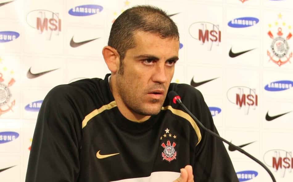 Jogador do Corinthians em coletiva de imprensa, diante do microfone, fundo com patrocinadores.