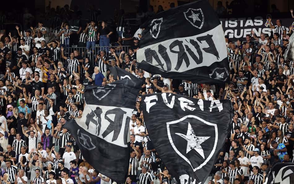 Torcida Fúria Jovem do Botafogo com bandeiras pretas e brancas, exibindo o escudo com estrela em estádio lotado.