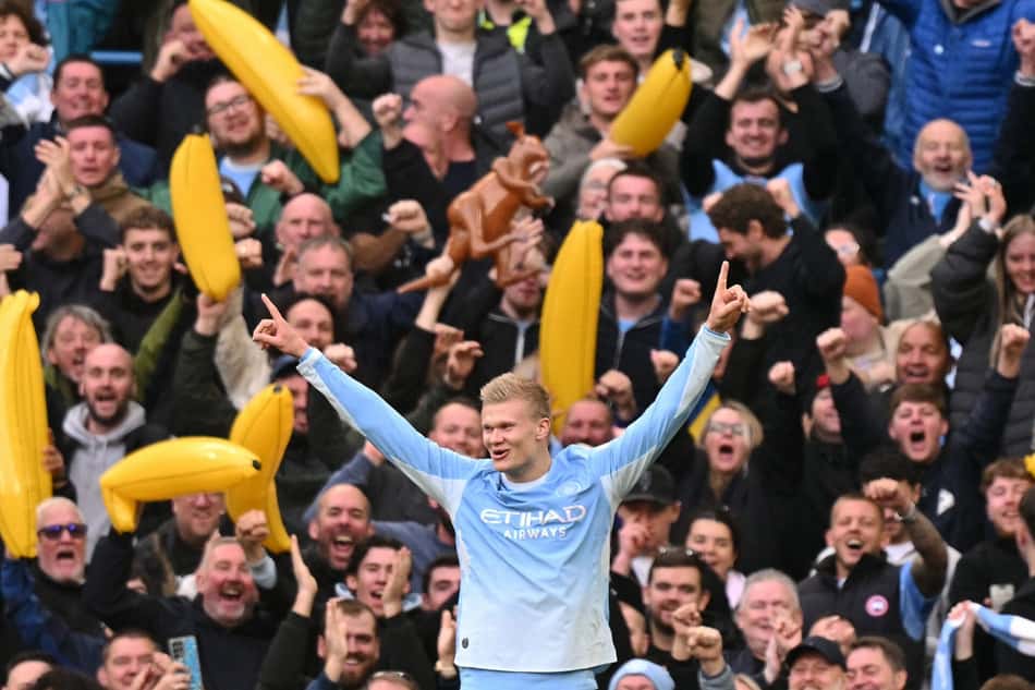 Jogador do Manchester City celebra vitória, cercado por torcedores com bananas amarelas.