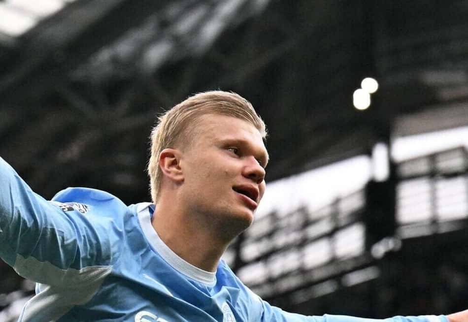 Jogador do Manchester City comemora gol com os braços abertos em estádio lotado.