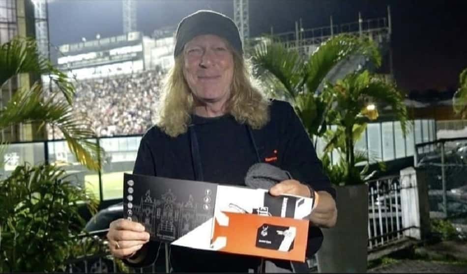 Janick Gers segurando folheto em show noturno, estádio com público lotado ao fundo