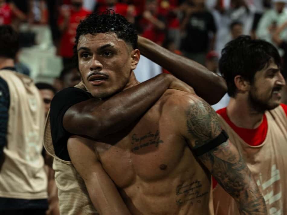 Dois jogadores celebram o abraço após o jogo, com torcida de vermelho ao fundo.