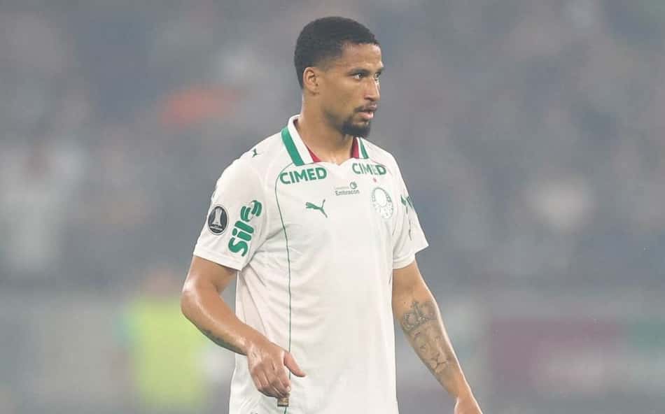 Murilo, zagueiro do Palmeiras, em campo com camisa branca e short verde.