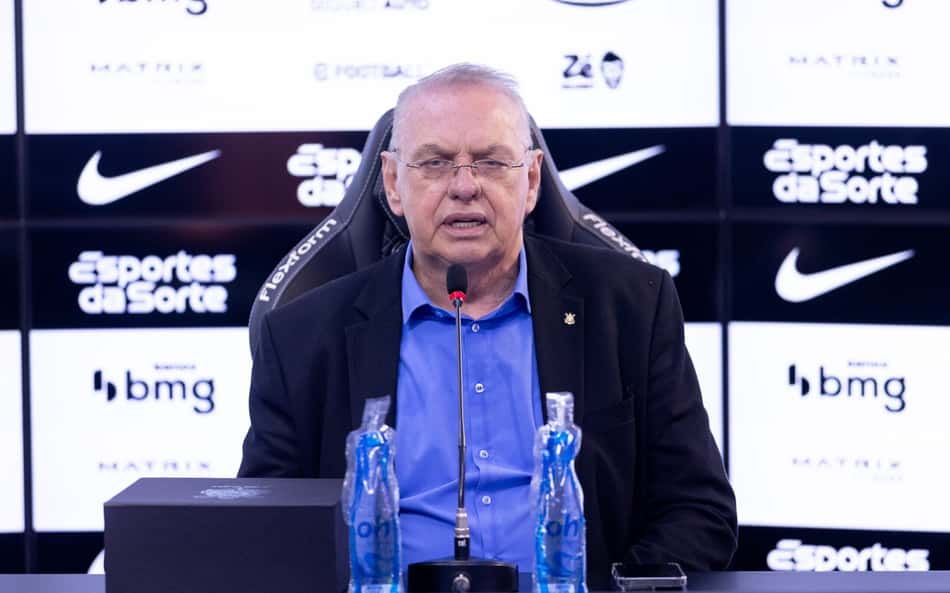 Osmar Stabile em coletiva de imprensa, sentado, com microfone, fundos com logos de patrocinadores.