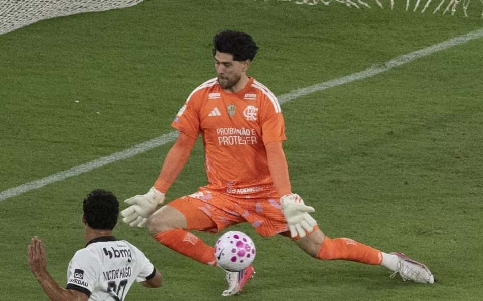 Goleiro de uniforme laranja defende chute em Flamengo x Atlético Mineiro, enquanto atacante branco avança.