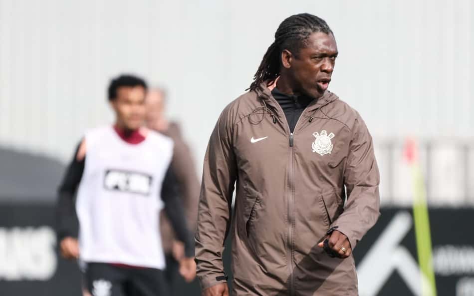 Clarence Seedorf em treino, casaco marrom com emblema da equipe, durante prática, com outro jogador ao fundo.