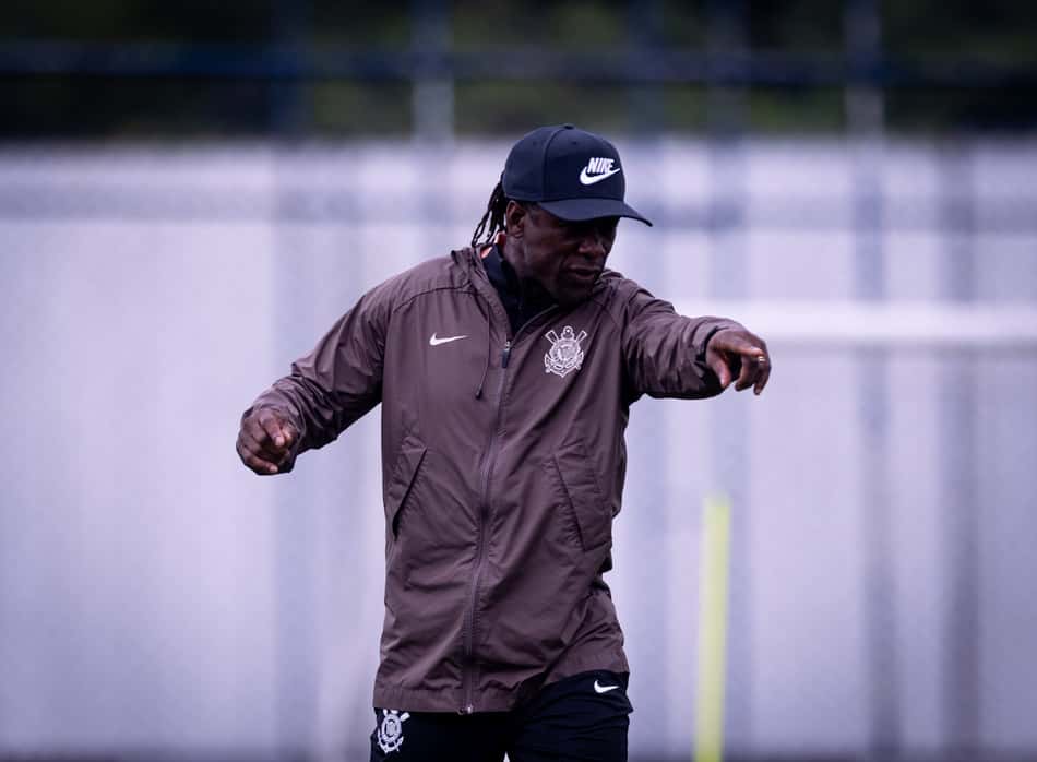 Clarence Seedorf treinando ao ar livre, vestindo jaqueta marrom e boné.