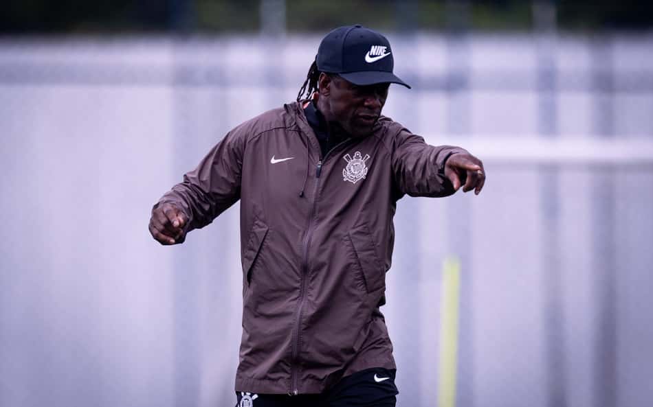 Clarence Seedorf treinando ao ar livre, vestindo jaqueta marrom e boné.