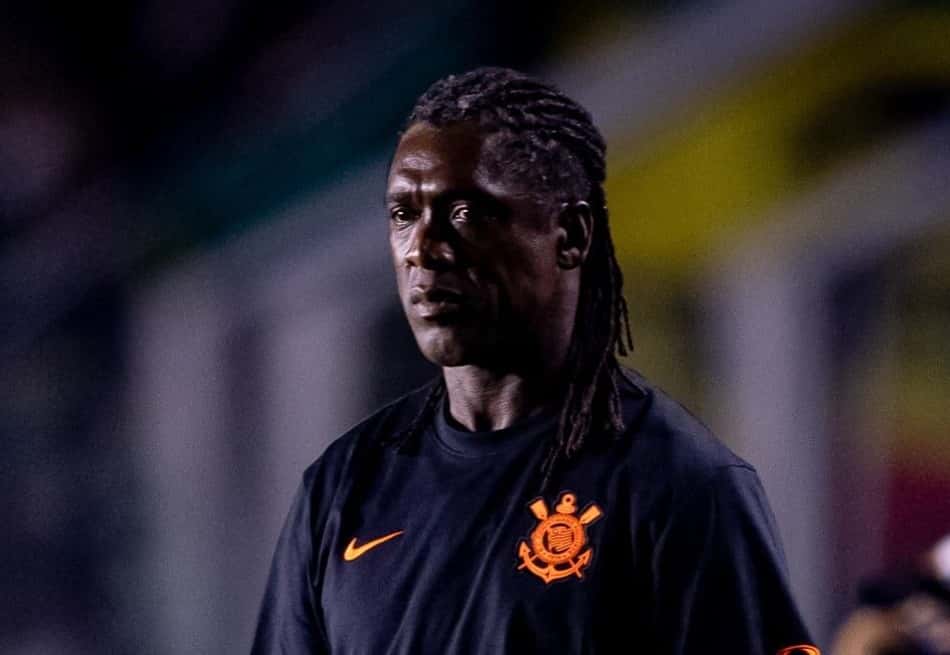 Seedorf, técnico, em uniforme preto com emblema laranja, em estádio ao fundo.
