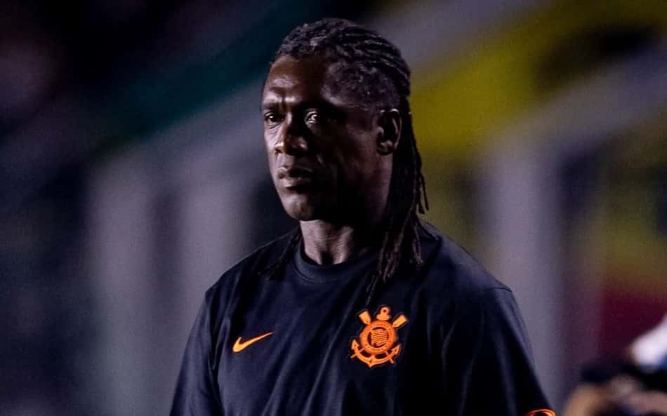 Seedorf, técnico, em uniforme preto com emblema laranja, em estádio ao fundo.