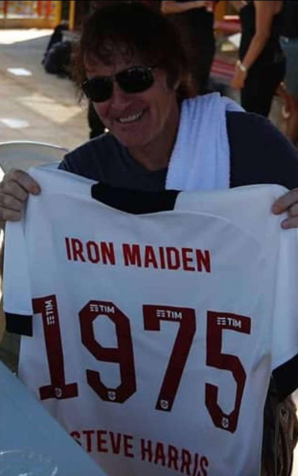 Homem com óculos escuros segura camiseta do Iron Maiden com o número 1975