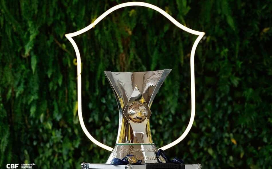 Taça Brasileirão em pedestal prateado, com moldura neon ao fundo e logotipo da CBF.
