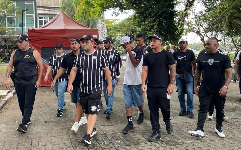 Torcida do Corinthians caminhando ao ar livre, com camisas pretas e listradas.
