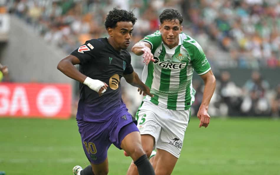 Yamal em duelo com jogador de uniforme verde e branco durante partida de futebol.