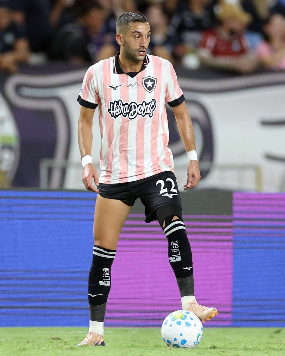 Hakim Ziyech em campo, camisa rosa e branca listrada, número 23, com a bola aos pés.