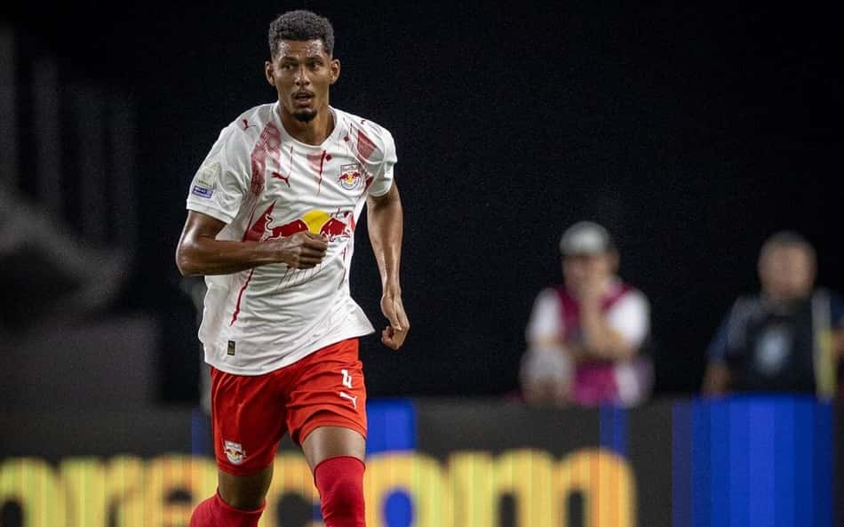 Jogador em uniforme branco com detalhes vermelhos controla a bola rosa em campo durante jogo noturno.