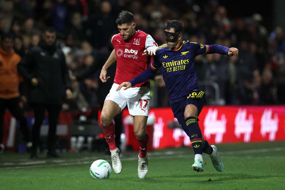 Arsenal enfrenta Fleetwood Town na Copa da Liga Inglesa; atacante em vermelho disputa a bola com o adversário de azul.
