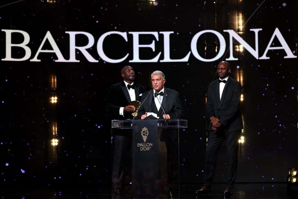 Cerimônia Ballon d'Or em Barcelona; palestrante no púlpito com dois homens de smoking ao lado.