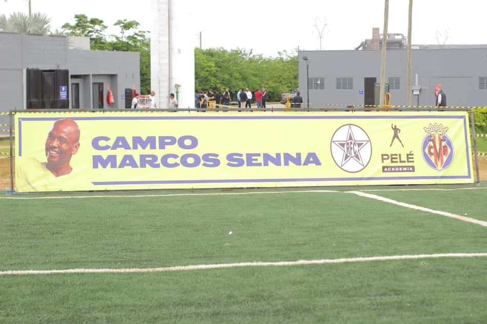 Banner do Campo Marcos Senna com retrato de Marcos Senna e logos da Pelé Academia, em campo de futebol