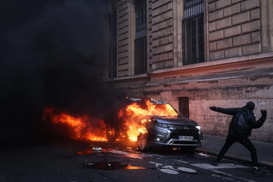 Manifestante arremessa um objeto em frente a um carro em chamas durante manifestação contra o alto custo de vida em Paris, na França, em 17 de outubro de 2026.