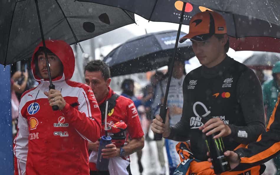 Charles Leclerc e Oscar Piastri se protegem, embaixo do guarda-chuva, da forte chuva do GP do Bahrein