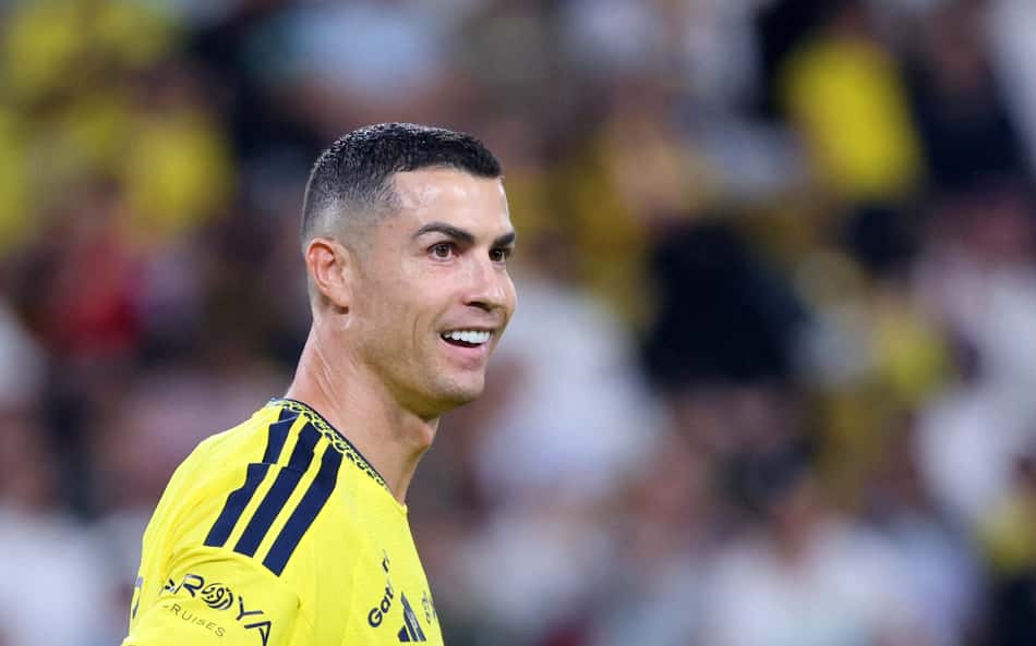 Cristiano Ronaldo sorrindo, vestindo uniforme amarelo com listras pretas nos ombros, em partida de futebol.