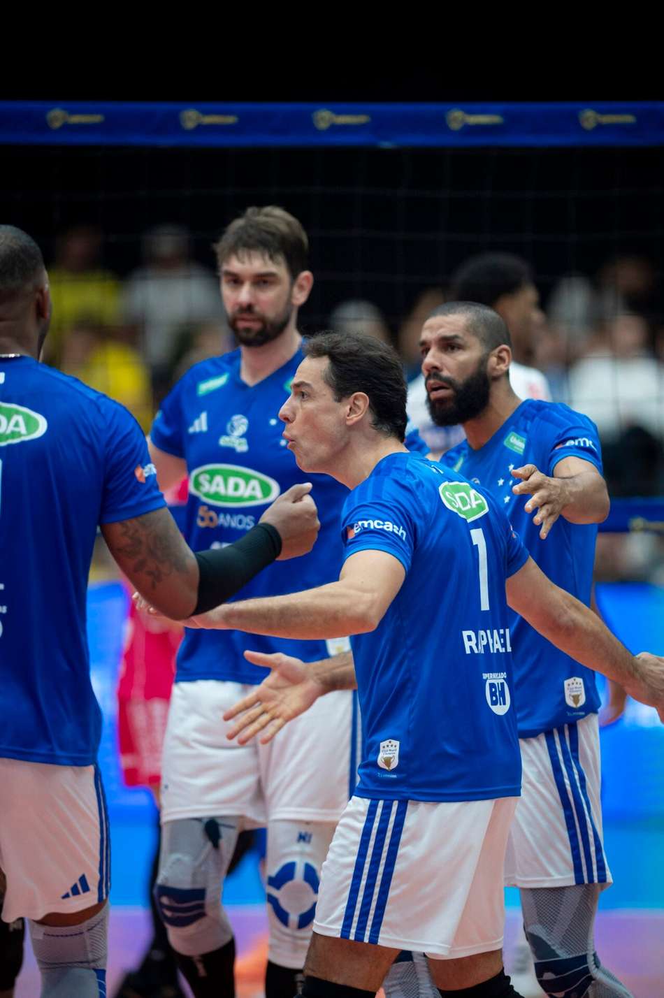 Jogadores do Cruzeiro Vôlei em uniforme azul celebram em quadra durante partida.