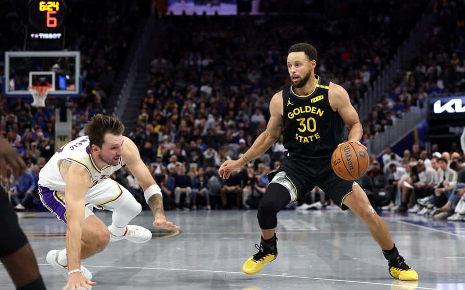 Stephen Curry (Golden State Warriors) com a bola contra Luka Dončić (Dallas Mavericks) em jogo da NBA.