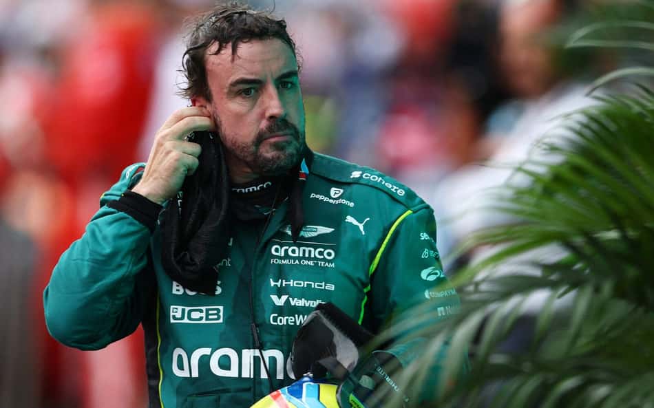 Fernando Alonso no GP dos EUA de Fórmula 1, com macacão da Aston Martin, retirando o rádio.
