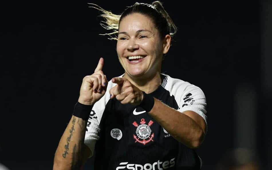 Jogadora do Corinthians sorri e aponta, com uniforme preto e o número 10