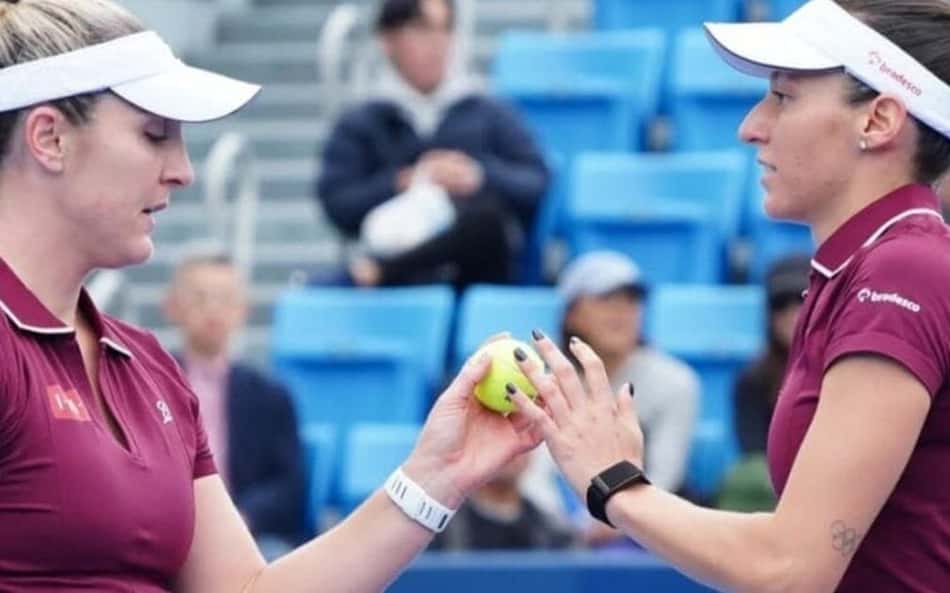 Gabriela Dabrowski e Luisa Stefani em quadra de tênis, trocando uma bola durante treino.