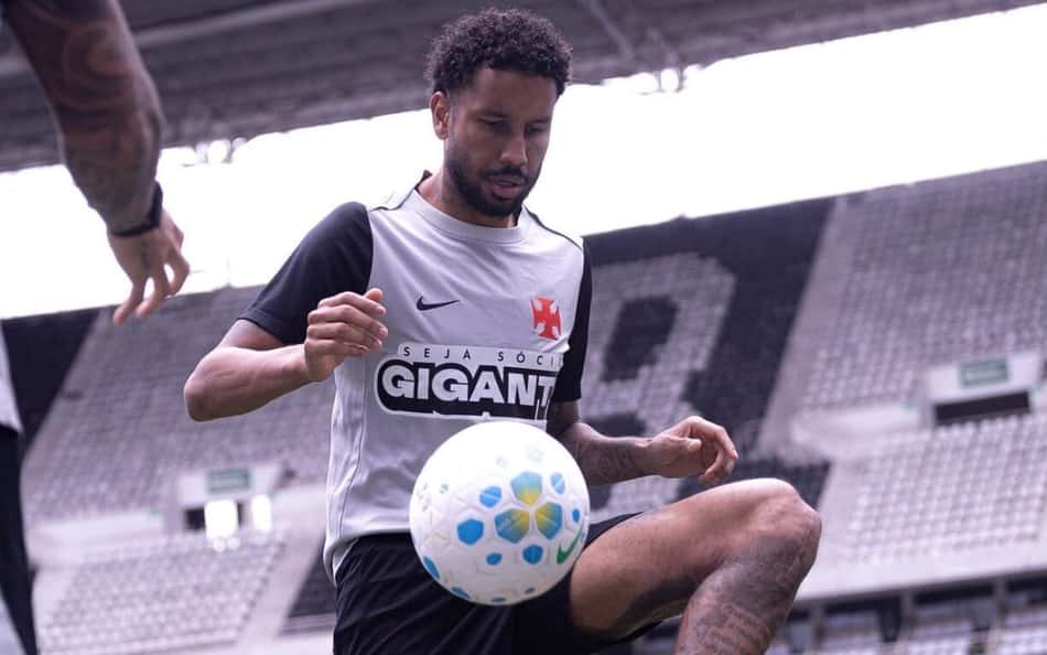 Jair treinando futebol em estádio, controlando bola azul, vestindo uniforme cinza com detalhes pretos.