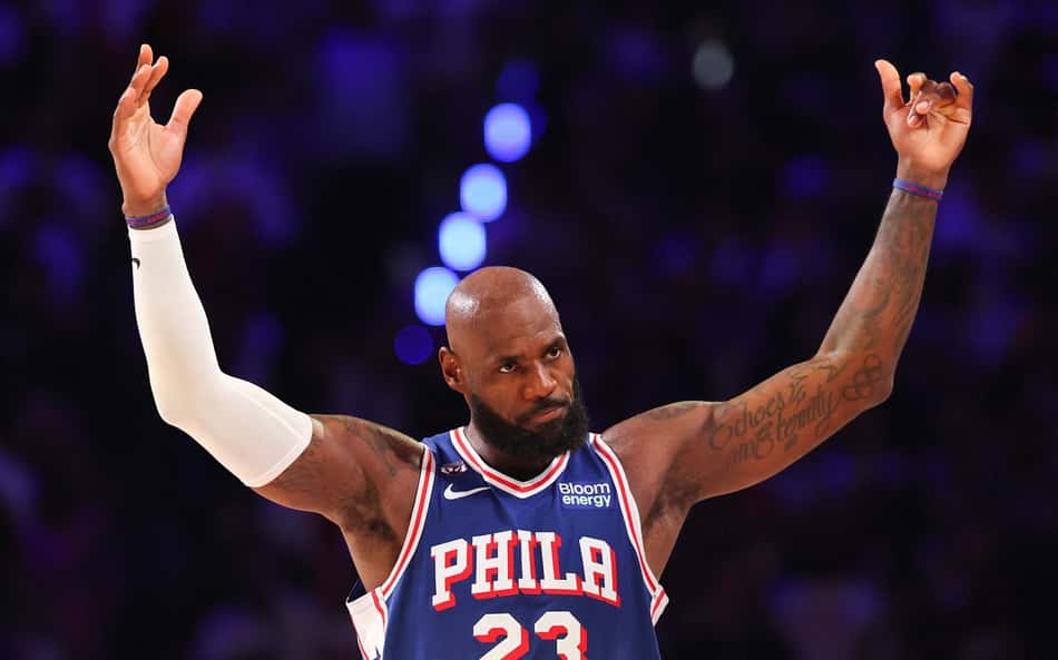 Jogador de basquete com tatuagens no braço, braços levantados, camisa azul PHILA nº23, em jogo da NBA.