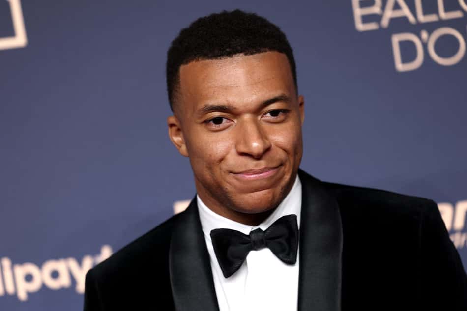 Kylian Mbappé no Ballon d'Or, sorrindo em smoking preto.