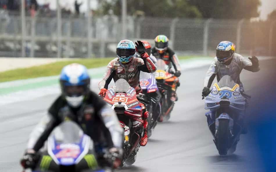 Grupo de pilotos de MotoGP na Phillip Island, GP da Austrália, acelerando na pista molhada.