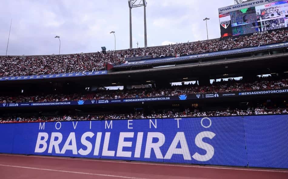 Torcida em estádio lotado, painel azul gigante com a frase MOVIMENTO BRASILEIRAS.