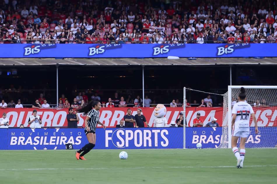 Jogadoras do Corinthians e São Paulo em campo pelo brasileirão feminino com placa do movimento brasileiras ao fundo