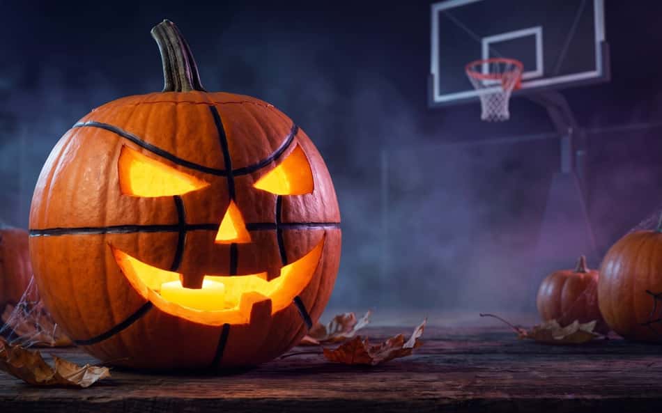 Abóbora esculpida iluminada em quadra de basquete, tema NBA Halloween, com outras abóboras e teias de aranha.