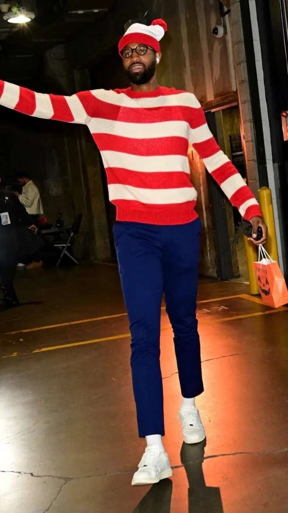 Homem com suéter vermelho e branco, gorro vermelho com pompon branco, óculos, calça azul e tênis brancos, sacola de Halloween(Foto: Divulgação)
