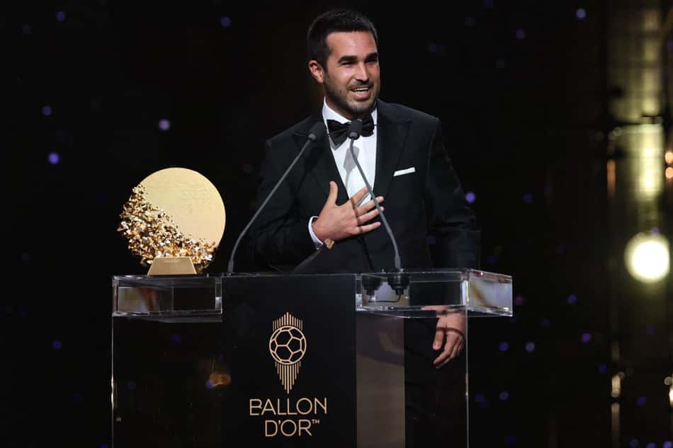 Pere Romeu no palco do Ballon d'Or, em terno preto, com a mão no peito, ao lado do troféu.