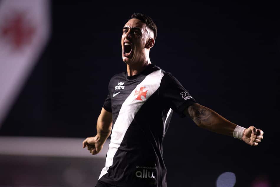 Jogador de futebol em camisa preta com faixa diagonal branca celebra, com o braço direito estendido.