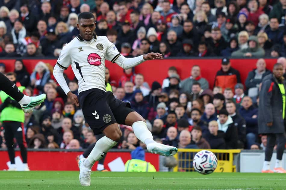 Jogador do Bournemouth chuta a bola durante a partida, com o estádio cheio ao fundo.