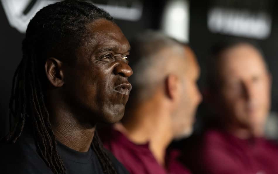 Clarence Seedorf em coletiva de imprensa, com dois colegas ao fundo.