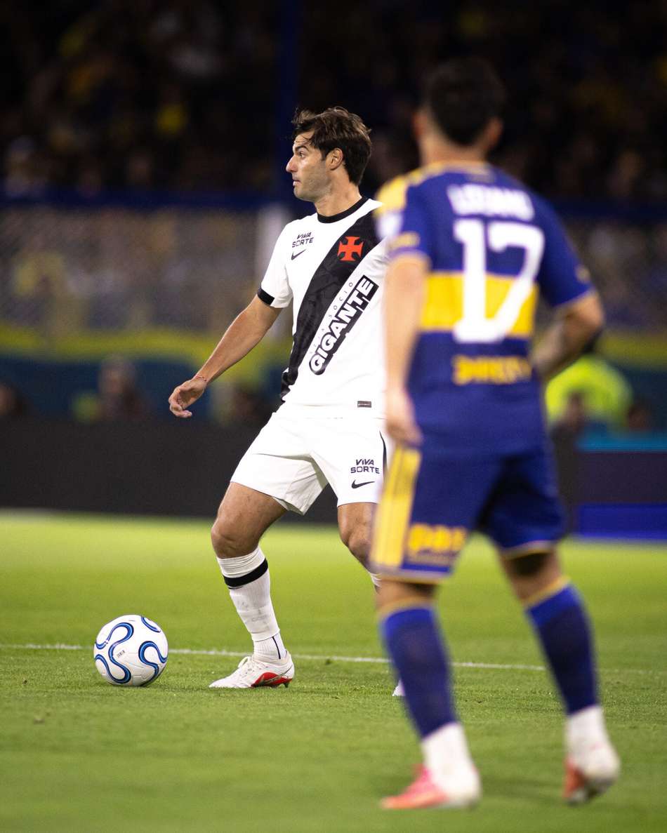 Jogador de camisa branca com faixa diagonal preta domina a bola em jogo contra adversário azul e amarelo.