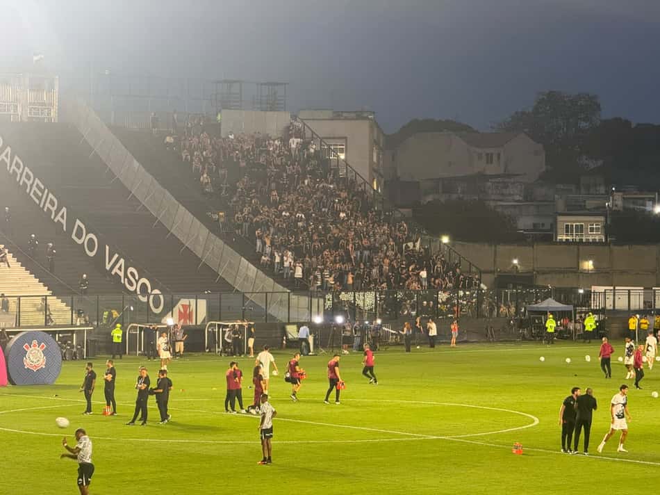 Torcida do Corinthians e Vasco da Gama em jogo da Brasileirão, arquibancadas cheias e jogadores aquecendo no campo.