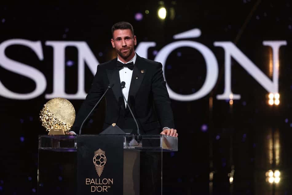 Homem em smoking no palco da cerimônia Ballon d'Or, ao lado do troféu dourado.