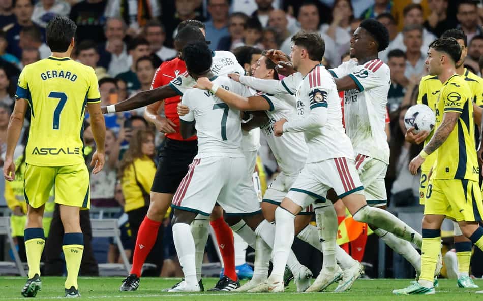 O atacante brasileiro do Real Madrid, número 07, Vinicius Junior (C), é contido por companheiros de equipe enquanto discute com o árbitro Isidro Escuderos após receber um cartão vermelho durante a partida do Campeonato Espanhol entre Real Madrid CF e Villarreal CF, no Estádio Santiago Bernabéu, em Madri, em 10 de outubro de 2026. (Foto: Oscar Del Pozo / AFP)