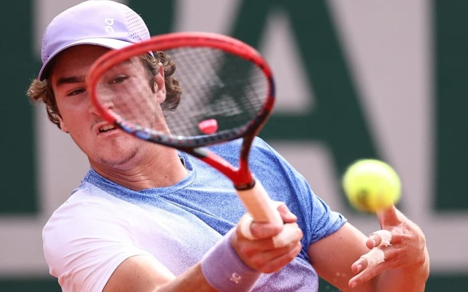 João Fonseca bate de direita na partida contra o francês Pierre-Hugues Herbert em Roland Garros (Photo by Anne-Christine POUJOULAT / AFP)