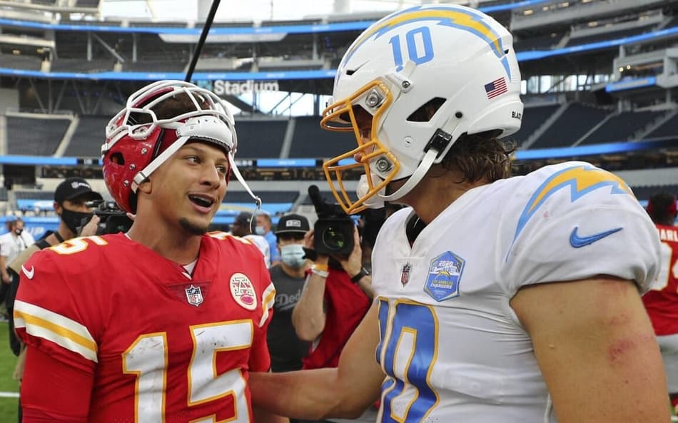 Patrick Mahomes dos Chiefs de vermelho olhando para Justin Herbert, dos Chargers, de branco e azul. Ambos Quarterbacks vão jogar na partida da NFl no Brasil