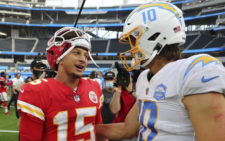 Patrick Mahomes dos Chiefs de vermelho olhando para Justin Herbert, dos Chargers, de branco e azul. Ambos Quarterbacks vão jogar na partida da NFl no Brasil